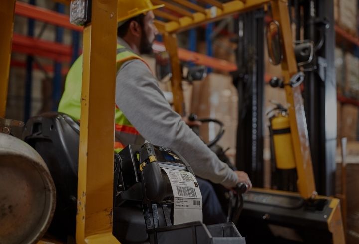 Warehouse worker driving forklift with label printer on the side